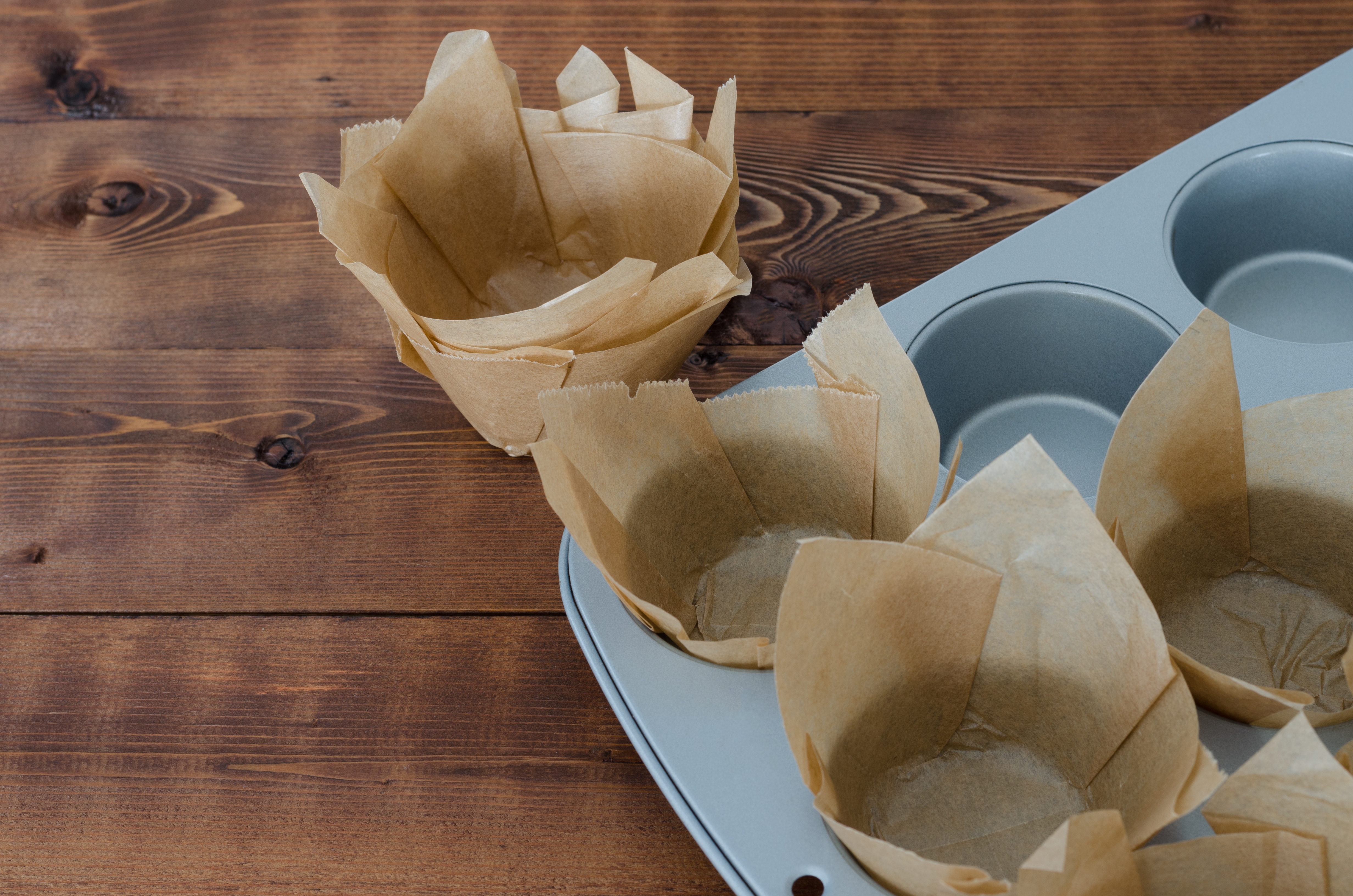 Muffin tin with unfilled, tulip-style paper liners on a wooden table