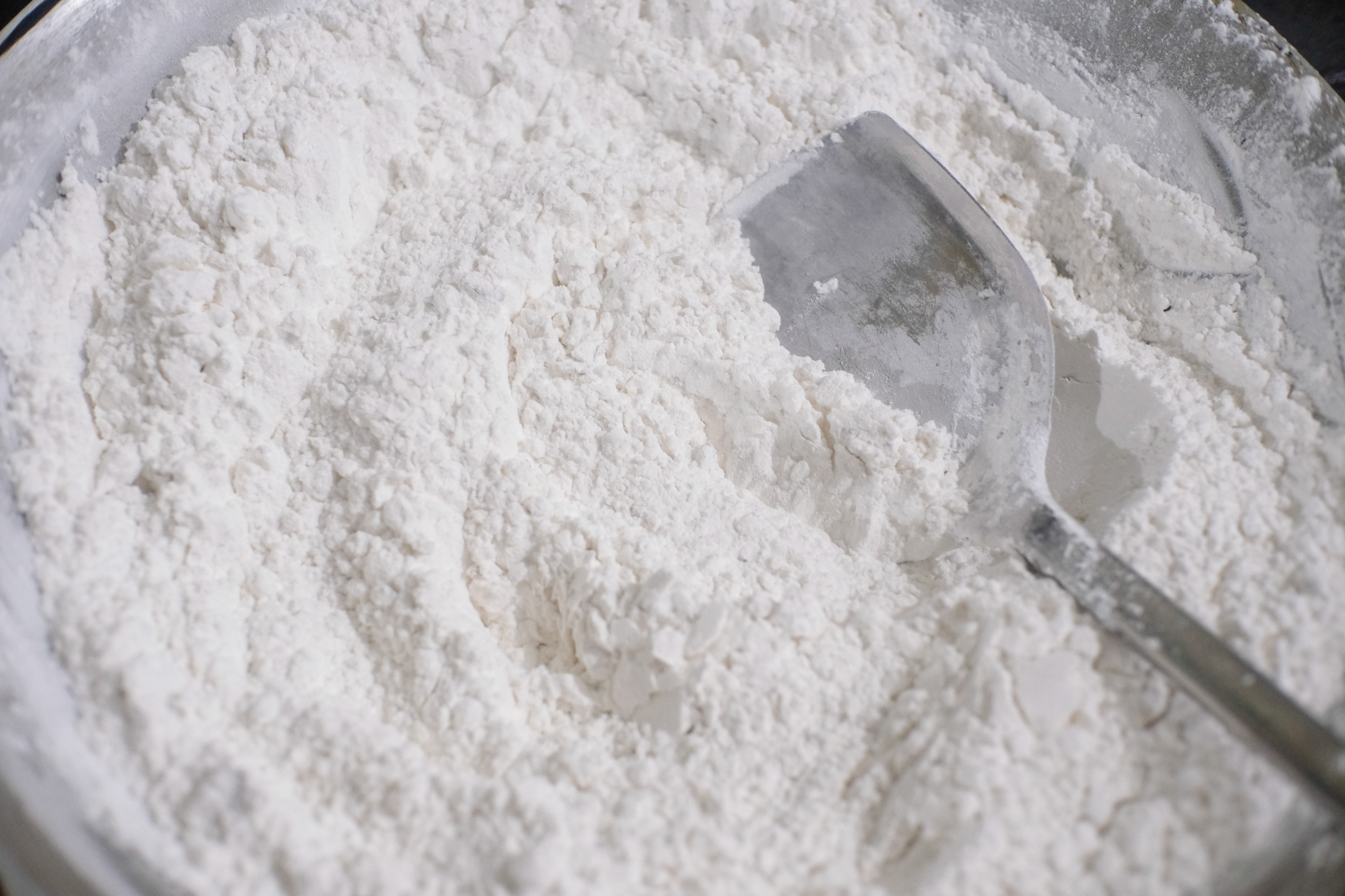 A metal scoop rests in a bowl filled with fine white flour, ready for baking or cooking
