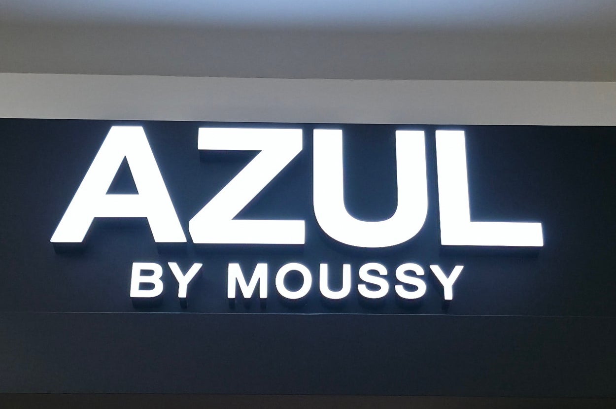 Storefront sign reading "AZUL BY MOUSSY" in bold, modern font above an entrance with ceiling lights visible