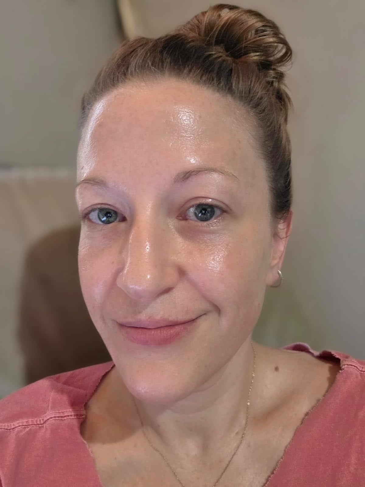 Person with a natural look, wearing a casual top and their hair in a bun, posing indoors