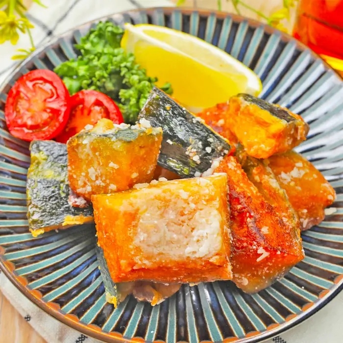 揚げたかぼちゃの角切りが皿に並べられ、トマト、レモン、パセリが添えられた料理。