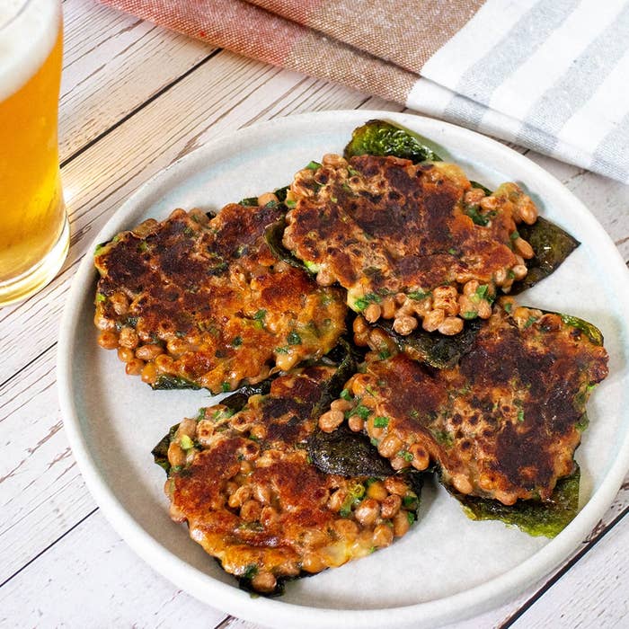お皿に載った納豆のお好み焼きと、横に置かれたグラスビール。日本の家庭料理の一例。