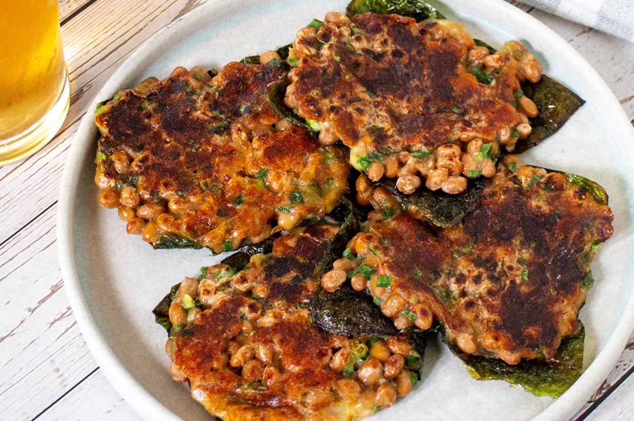 皿に盛られた納豆と青菜のチヂミ風料理と、横に置かれたグラスビール。