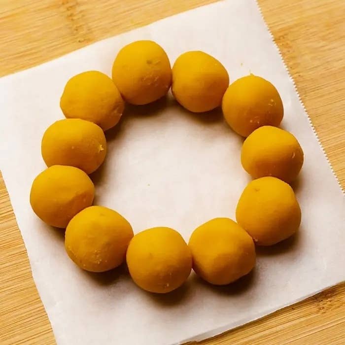 円形に並べられた10個の球状の黄色いスイーツが、白い紙と木の背景に置かれている。