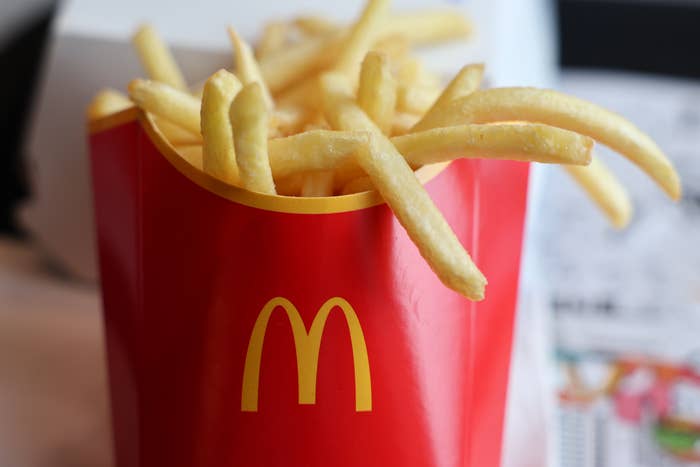 Fries in a McDonald's carton, placed on a table next to a tray with part of a paper liner visible in the background