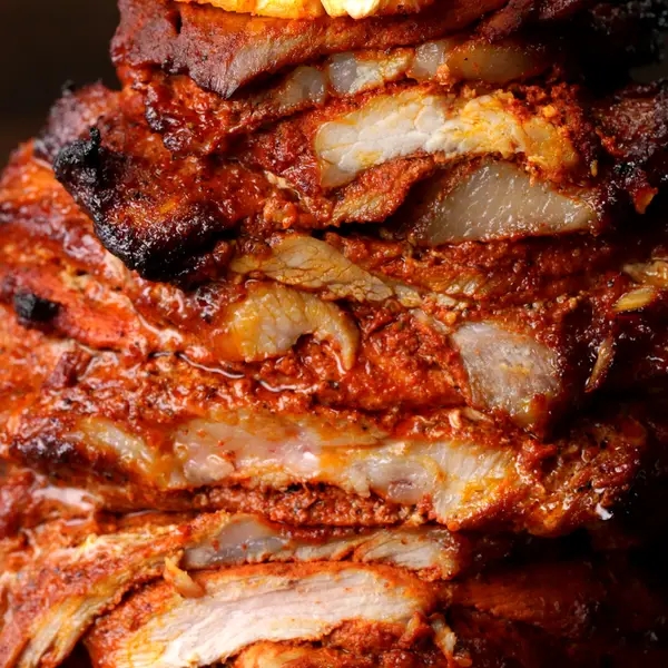 Close-up of stacked, marinated, and grilled meat slices, showcasing a juicy and tender texture, likely prepared for tacos or similar dishes