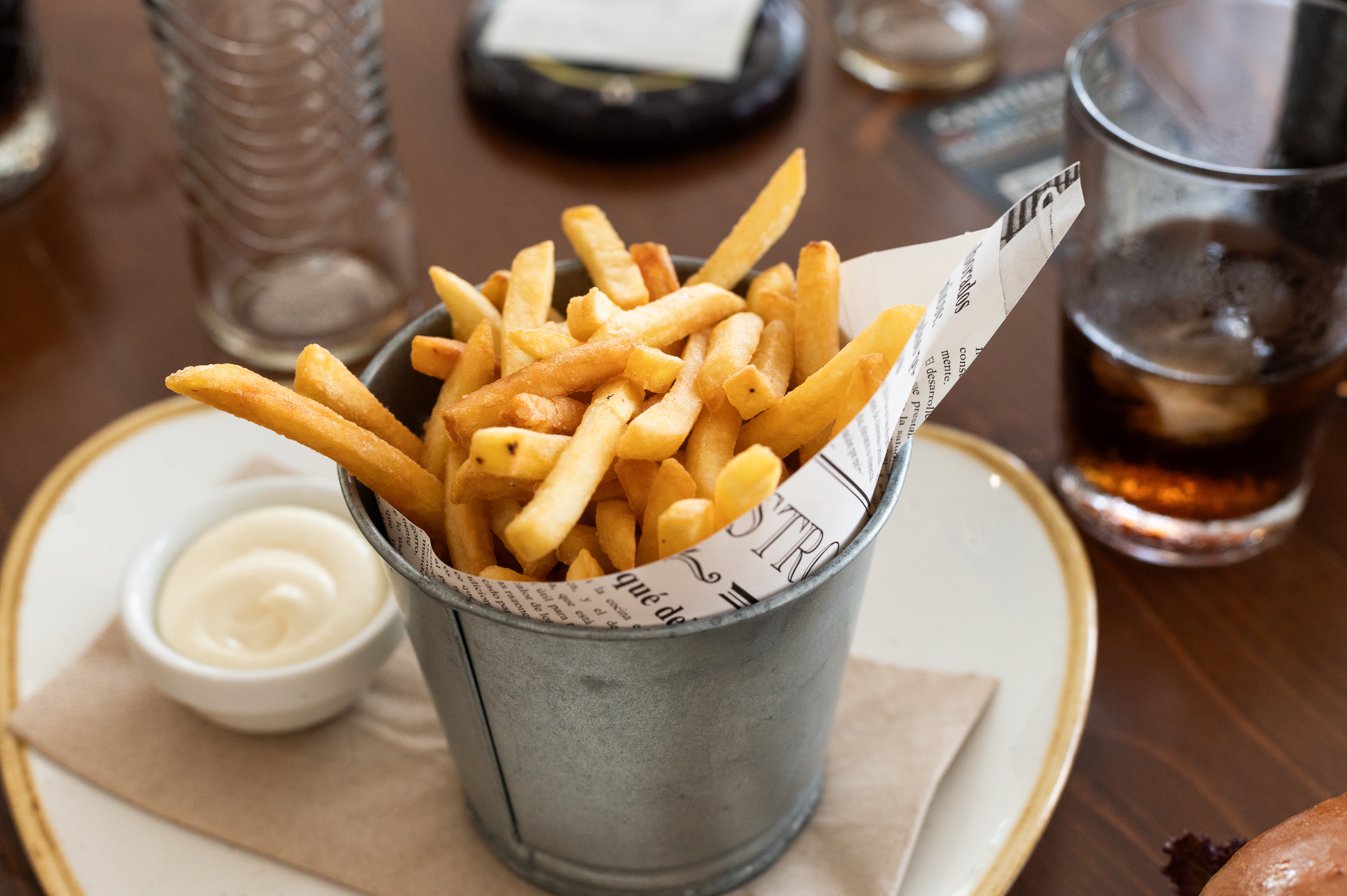Fries served in a metal bucket with a side of dipping sauce on a table setting