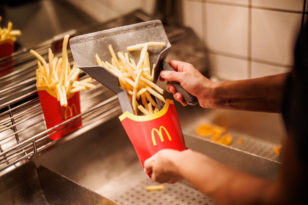 A person places freshly cooked fries into a red McDonald's box at a fast-food restaurant