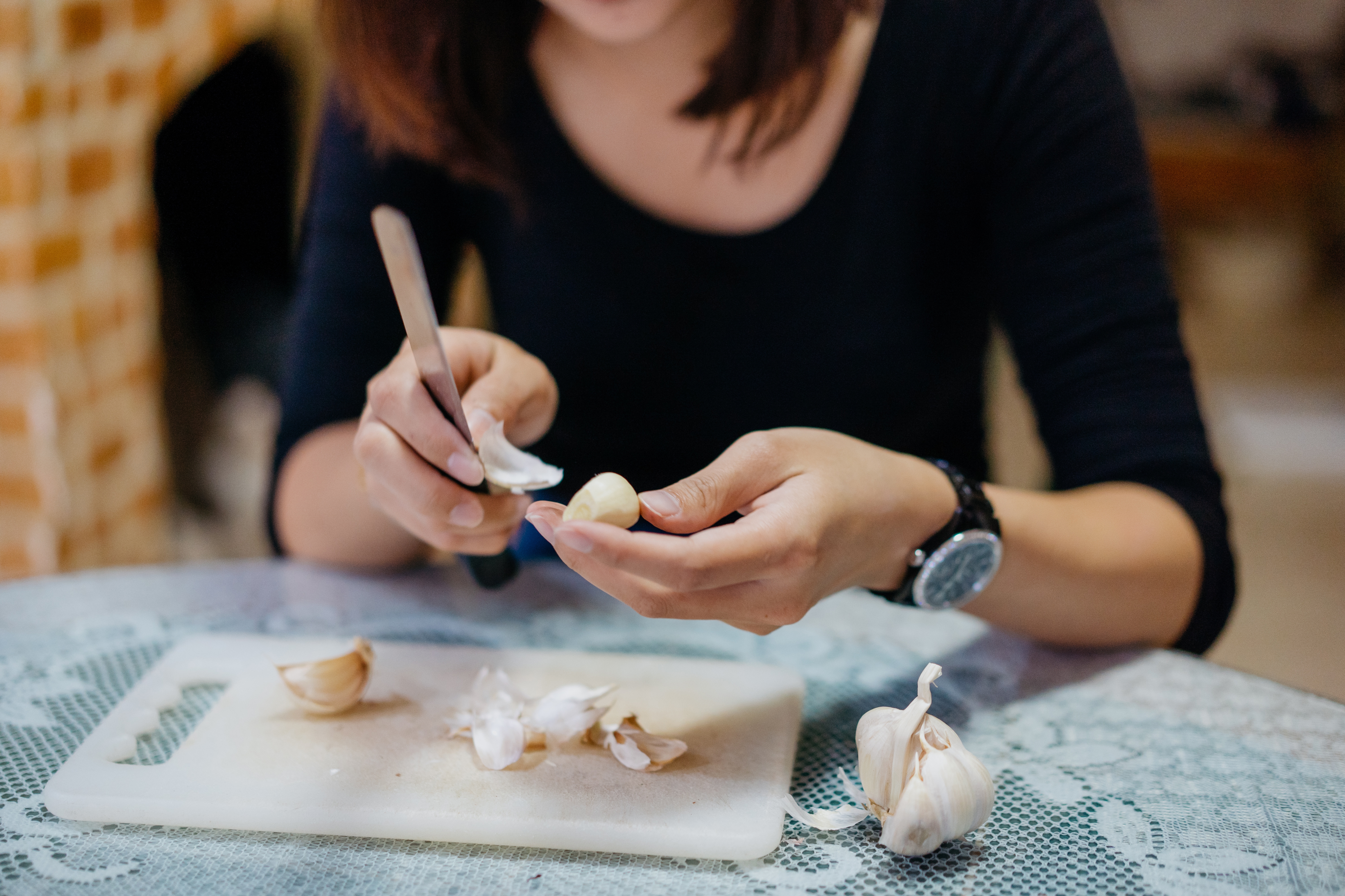 Person skreller hvitløksfedd ved et bord med kniv, fokus på hender og hvitløk