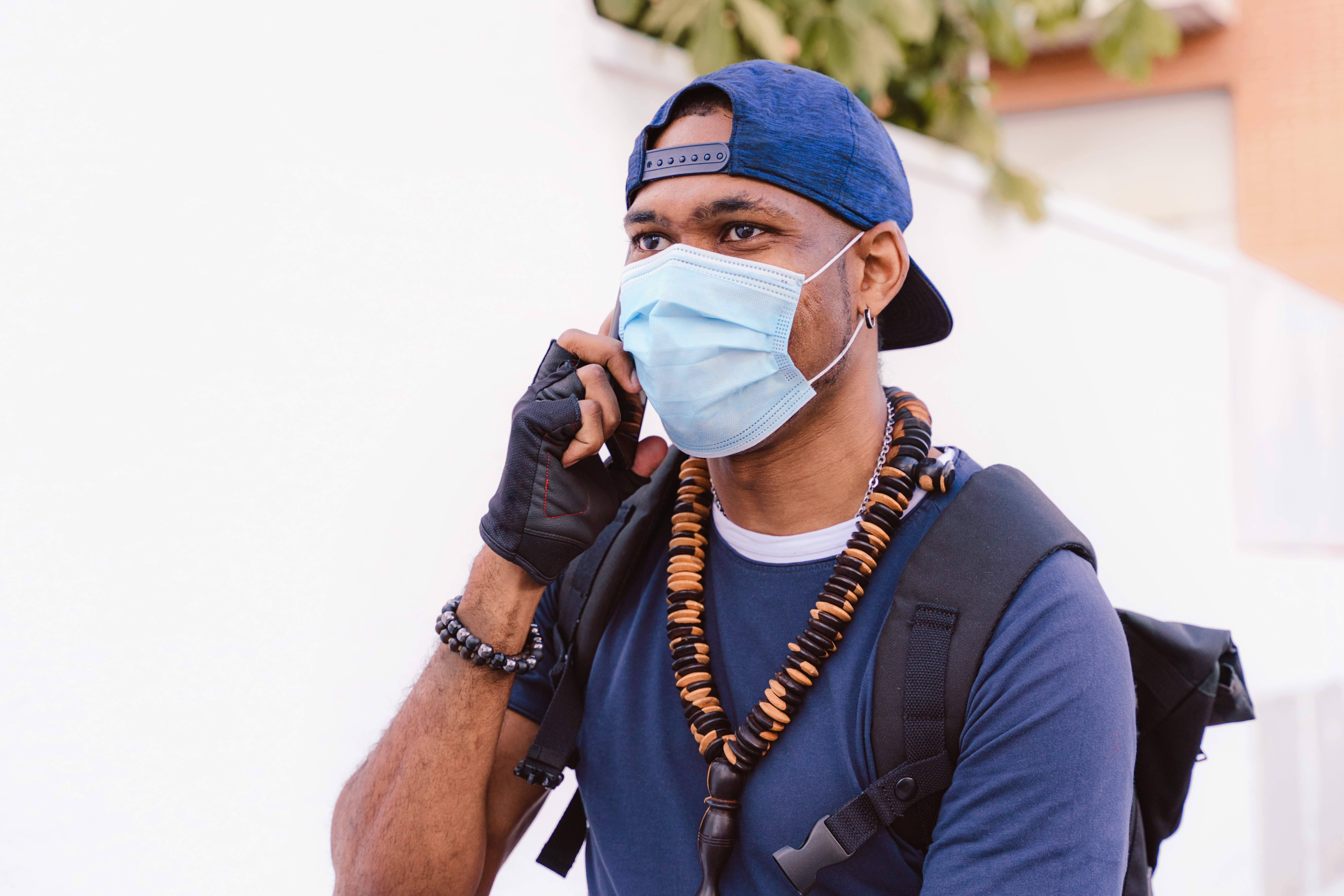 Person som har en ansiktsmaske, hette og uformell antrekk med en ryggsekk og perlet halskjede, og snakker i telefonen utendørs