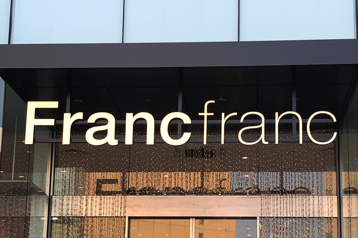 Francfrancの店舗入口。モダンなガラスと金属のファサードが見え、背景に都市の建物が並ぶ。