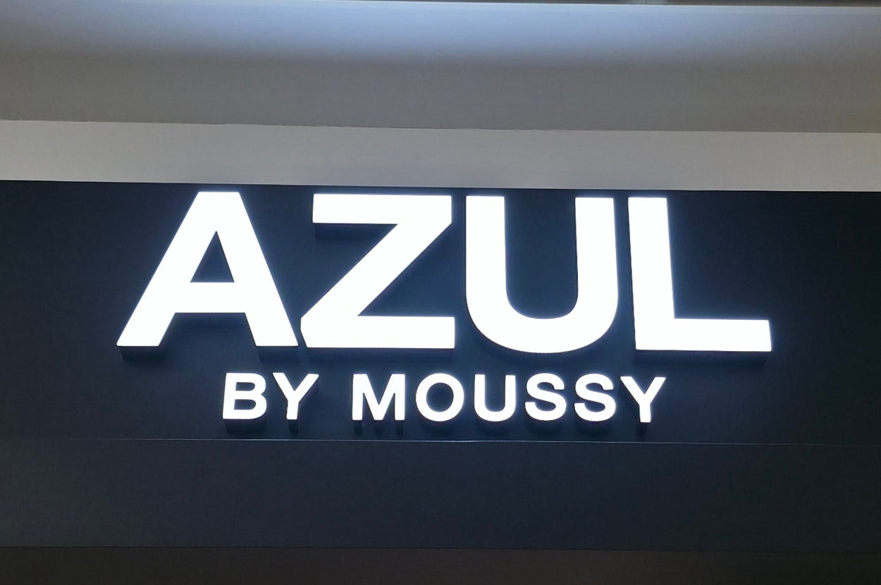 Store sign reading "AZUL BY MOUSSY" in bold, lit letters on a dark background. Ceiling lights and vents are visible above