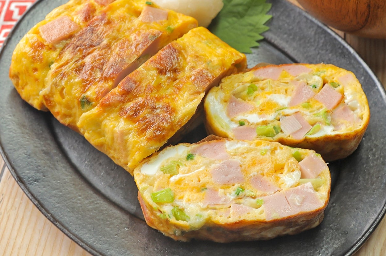 厚焼き卵が黒い皿に盛られ、ハムとネギが入っている。横には大根おろしと味噌汁の椀がある。