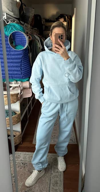 Person successful a cozy hoodie and sweatpants stands successful a closet, taking a reflector selfie.
