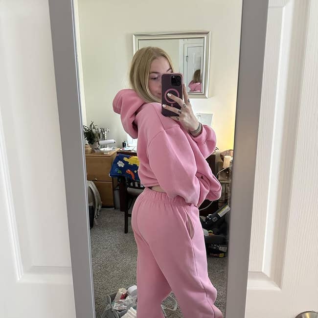 Person wearing cozy, oversized pinkish hoodie and sweatpants, taking a reflector selfie successful a casual location setting