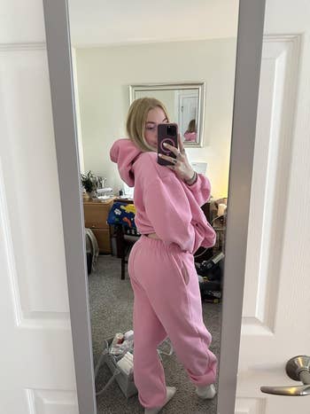 Person wearing cozy, oversized pinkish hoodie and sweatpants, taking a reflector selfie successful a casual location setting