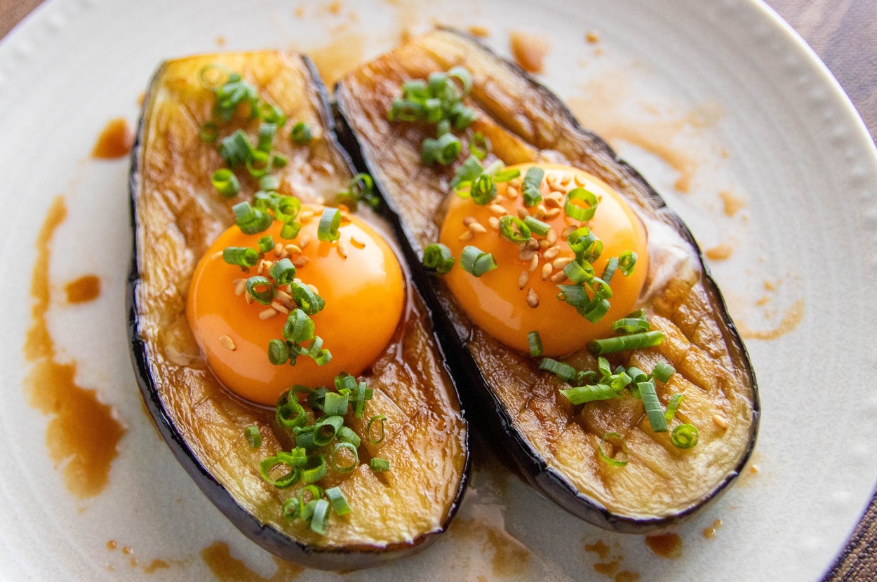 皿に盛られたナスの上に生卵とネギがのっている料理。