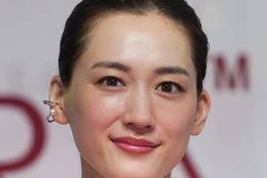女性が微笑んでカメラを見つめています。シンプルなデザインのシャツを着ています。