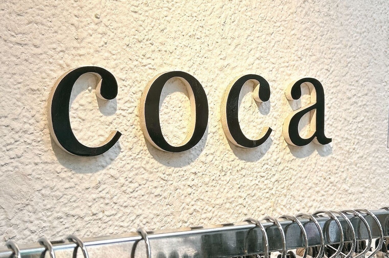 服のハンガーラックの上に「coca」と書かれた店の看板。