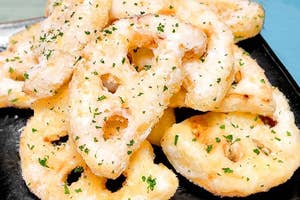 揚げたレンコンチップスが黒い皿に盛られている。細かい緑のハーブがトッピングされている。