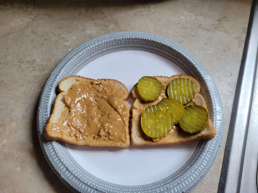 Two slices of toast on a plate, one with peanut butter and the other with pickle slices
