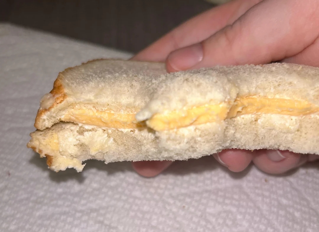 A hand holding a plain cheese sandwich made with crustless white bread, over a paper towel