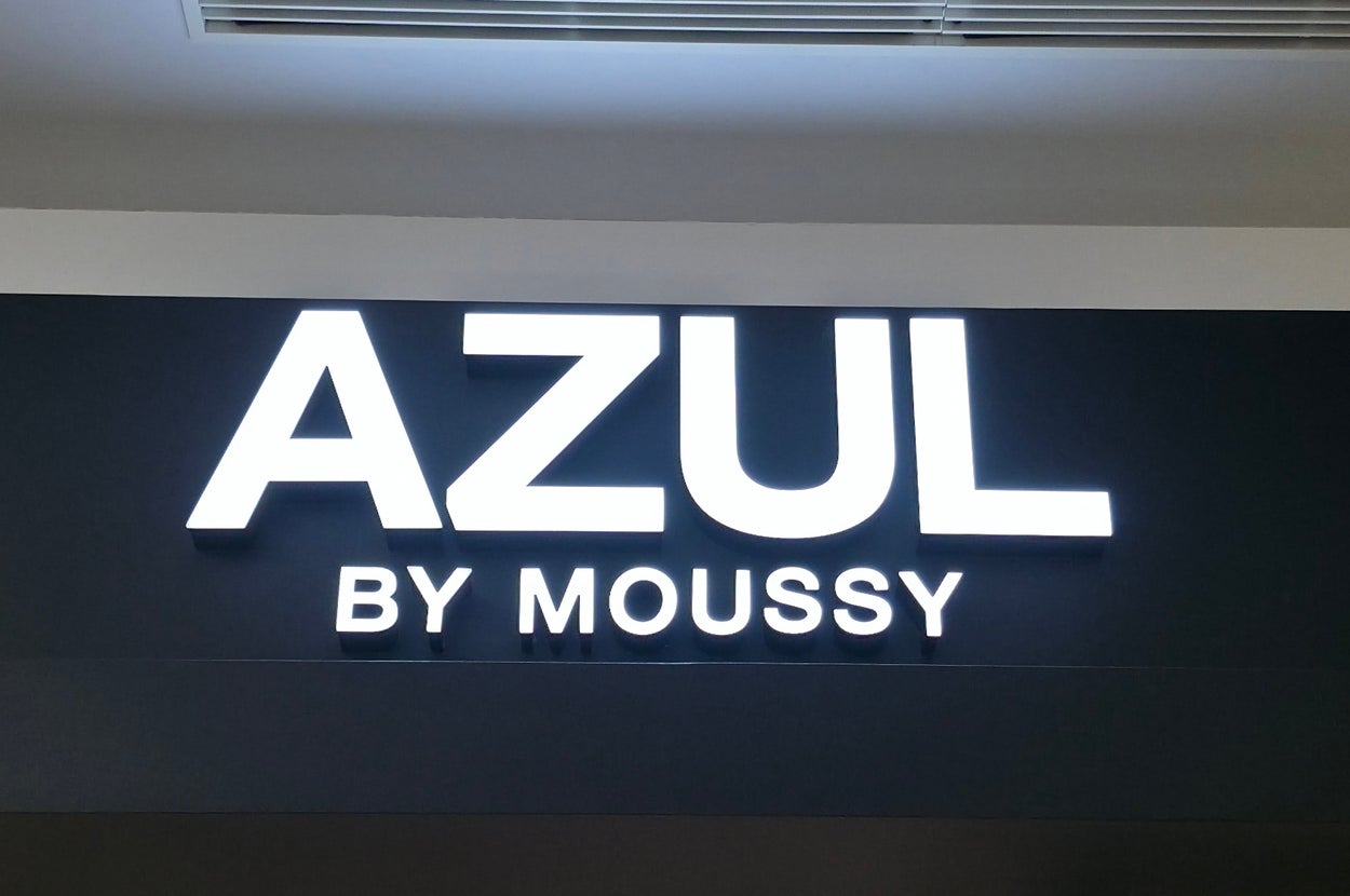 Store sign reading "AZUL BY MOUSSY" beneath a ceiling vent and lights