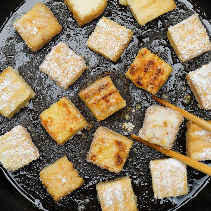 フライパンで焼かれた複数の豆腐の角切りを箸でひっくり返している。