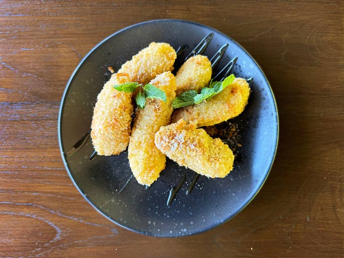 A plate of golden-brown breaded food, garnished with fresh mint leaves, served on a dark plate atop a wooden table