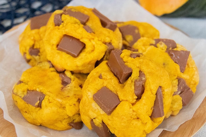 プレートに盛られたチョコレートチャンク入りのかぼちゃクッキー。背景にかぼちゃの一部が見える。
