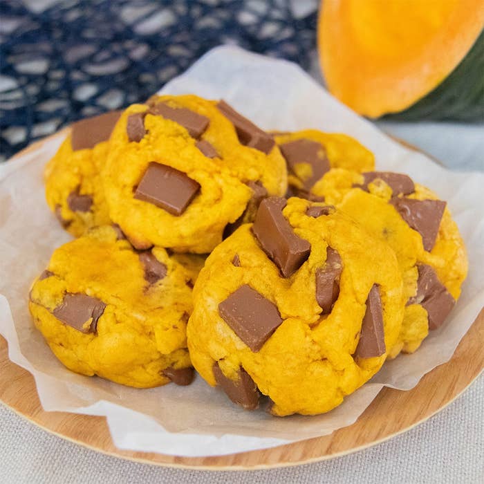 プレートに盛られたチョコレートチャンク入りのかぼちゃクッキー。背景にかぼちゃの一部が見える。