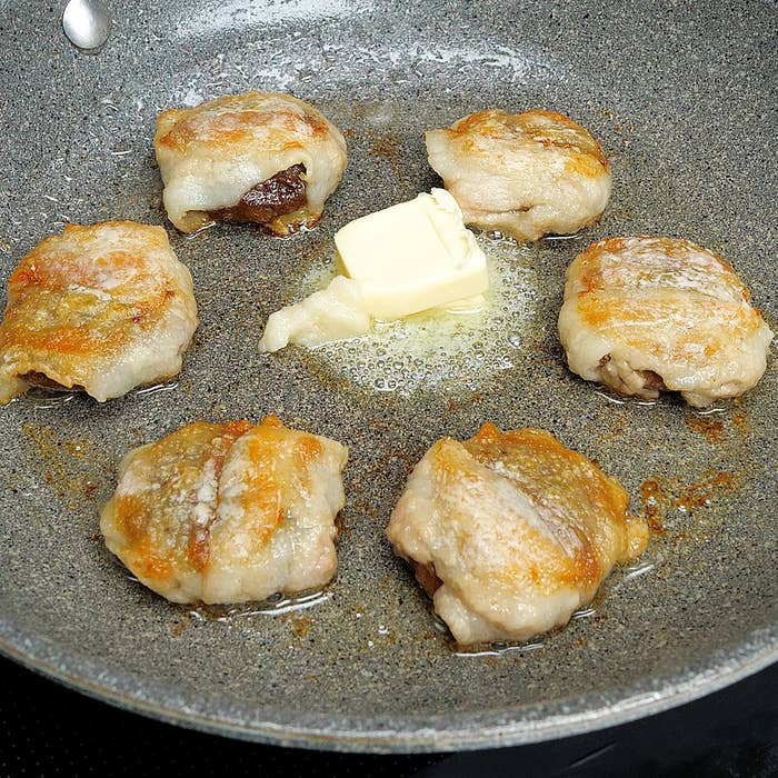 フライパンでバターと一緒に焼かれているしいたけの肉巻き。