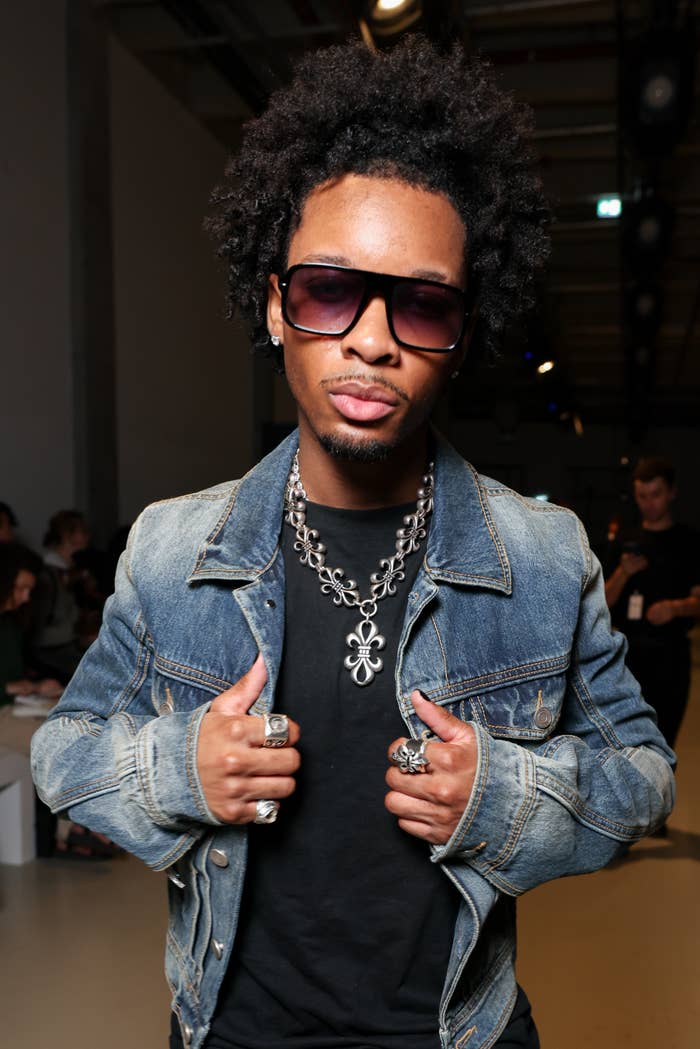 Individual wearing sunglasses, a denim jacket, and layered chain necklaces at a music-related event