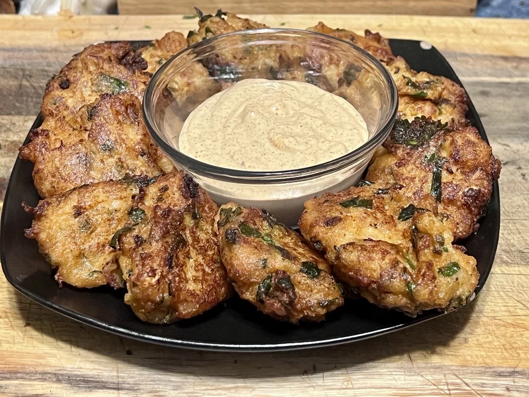 Plate of crispy vegetable fritters arranged around a bowl of creamy dipping sauce on a square black dish