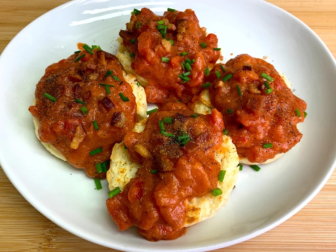 Biscuits topped with savory tomato gravy and sprinkled with chopped chives on a white plate