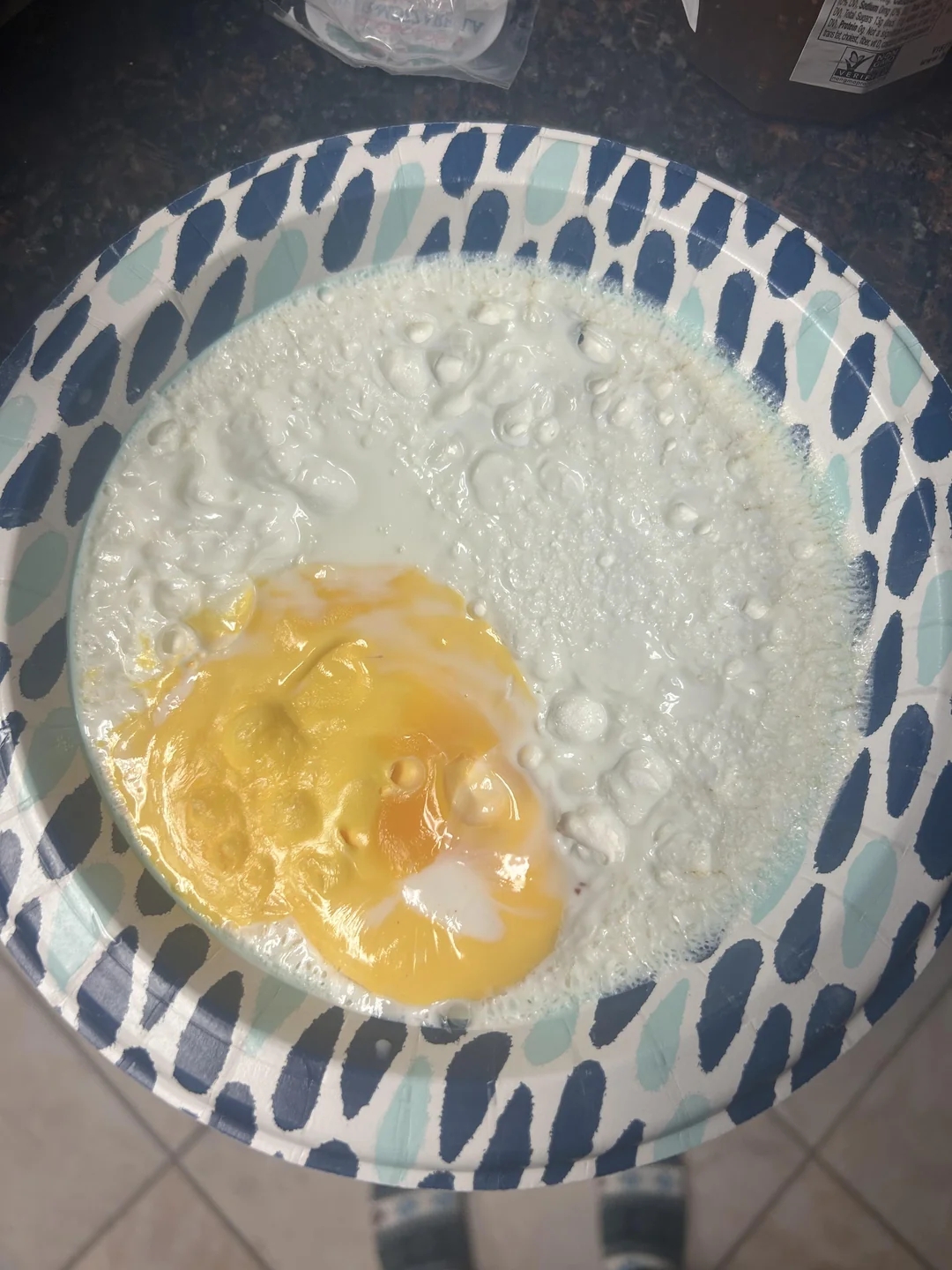 Egg yolk and egg white in a paper bowl ready to be mixed, shown on a kitchen countertop