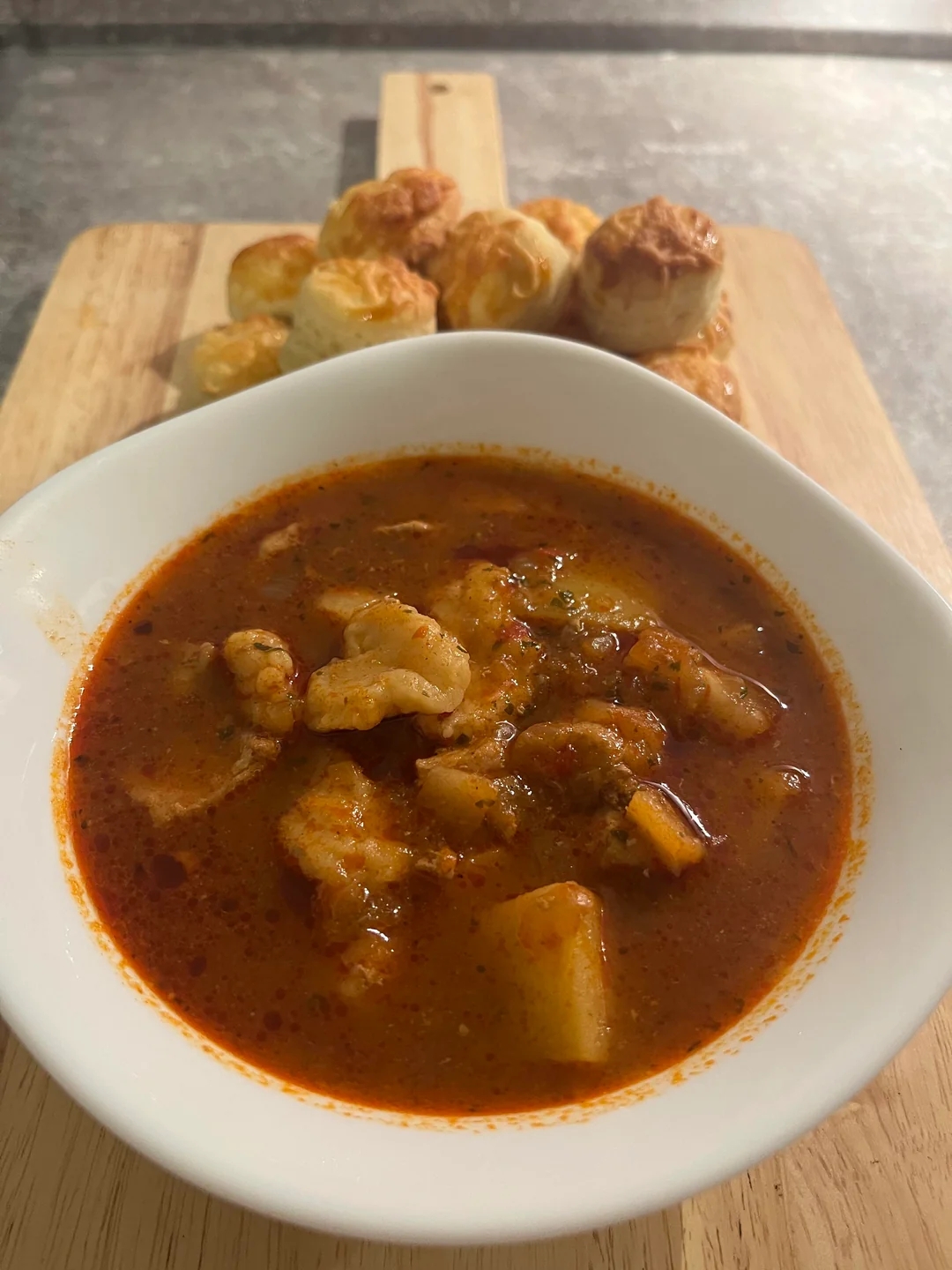 Bowl of hearty stew with vegetables and chunks of meat, served alongside a wooden board with puff pastry bites