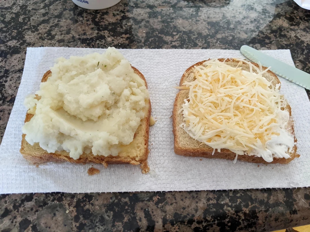 Two slices of bread with mashed potatoes on one and shredded cheese on the other, on a paper towel on a countertop