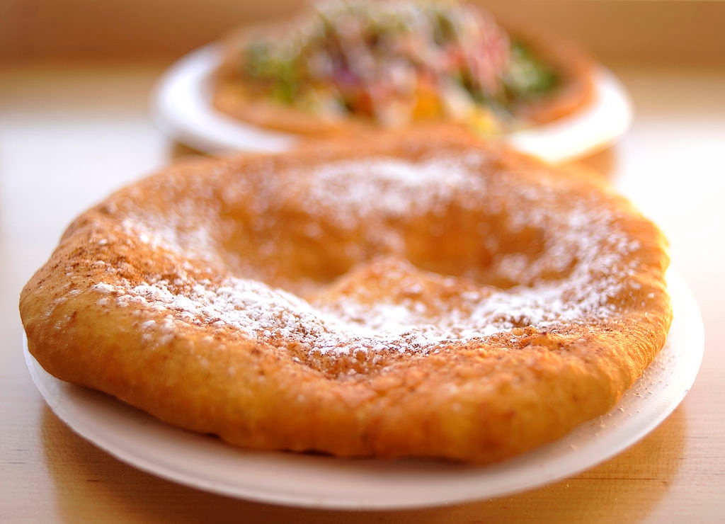 Fried dough dusted with powdered sugar on a plate, with a blurred dish of salad in the background