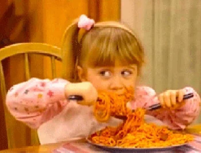 Child eagerly eating a large plate of spaghetti using a fork and spoon at a dining table