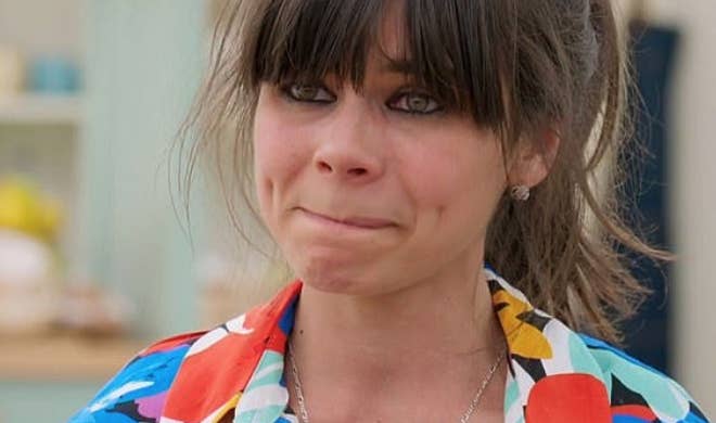 A person with long hair and bangs appears emotional. They are wearing a colorful, patterned shirt in a casual setting
