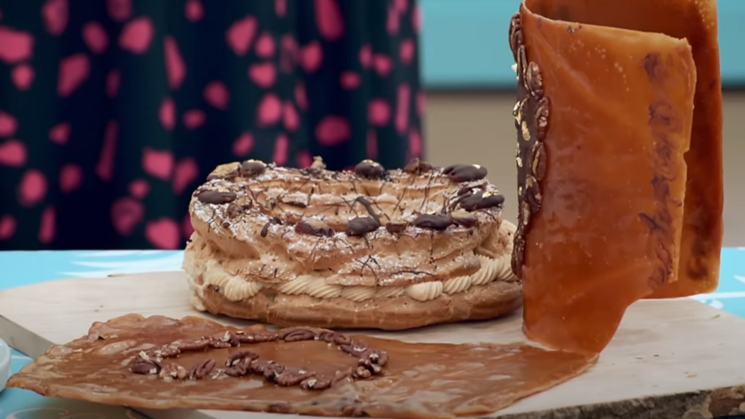 Elaborate pastry with layered cream filling and decorated with chocolate details next to caramel sheets on a wooden board