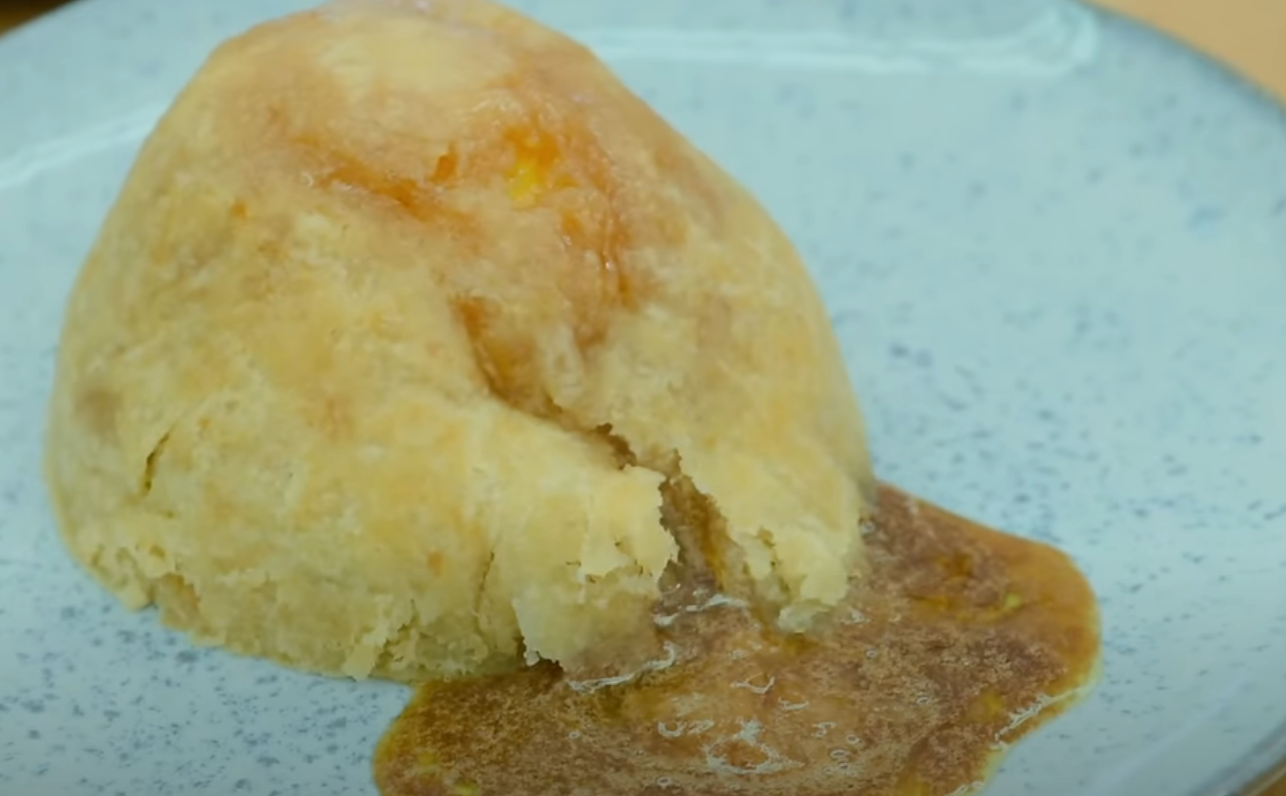 A dome-shaped steamed pudding on a plate with sauce oozing out