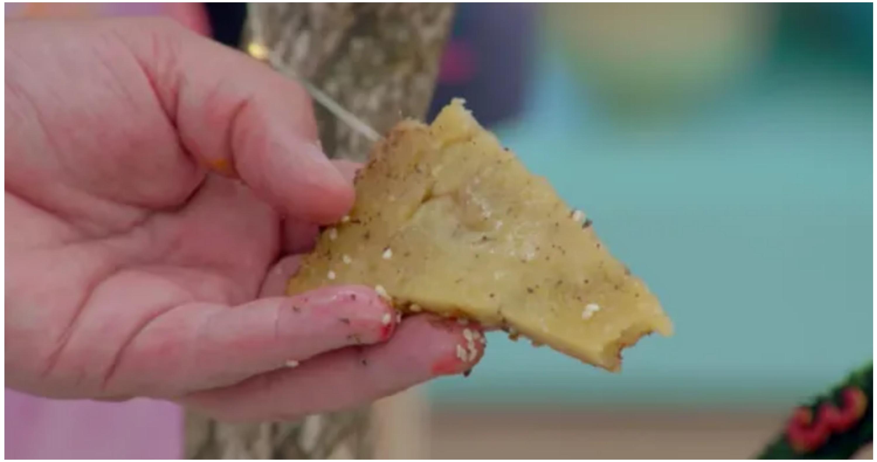 A hand holding a small triangular slice of pie topped with seasoning