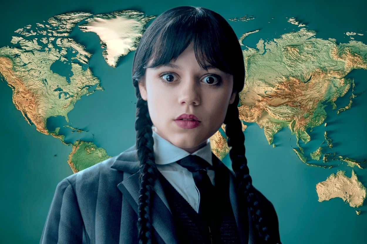 Person with braided hair and formal attire poses against a world map backdrop with a surprised expression