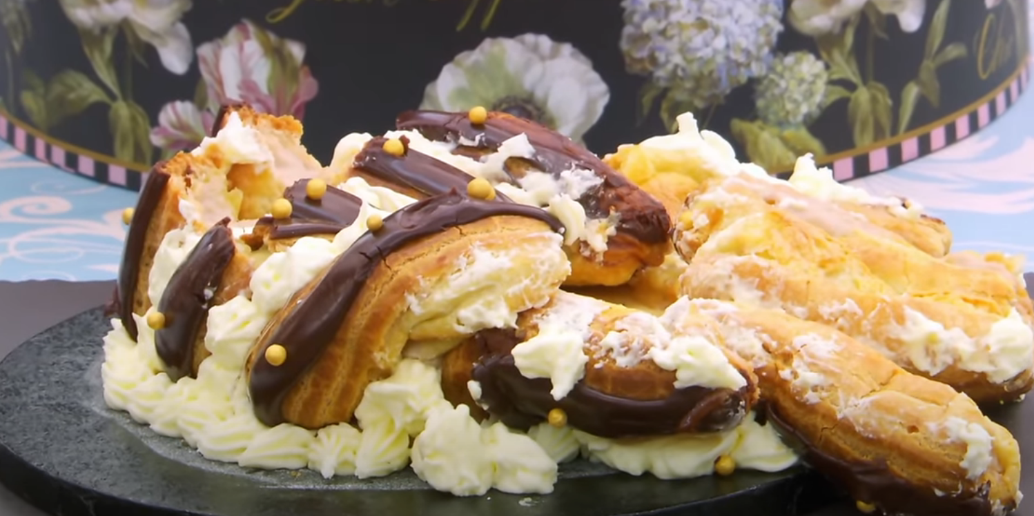 A display of cream-filled eclairs, some topped with chocolate and small decorative beads, arranged on a platter