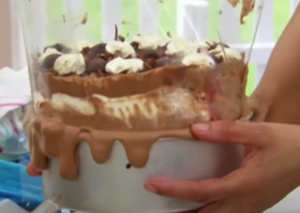 Messy layered dessert with dripping chocolate and whipped cream, being held by a person