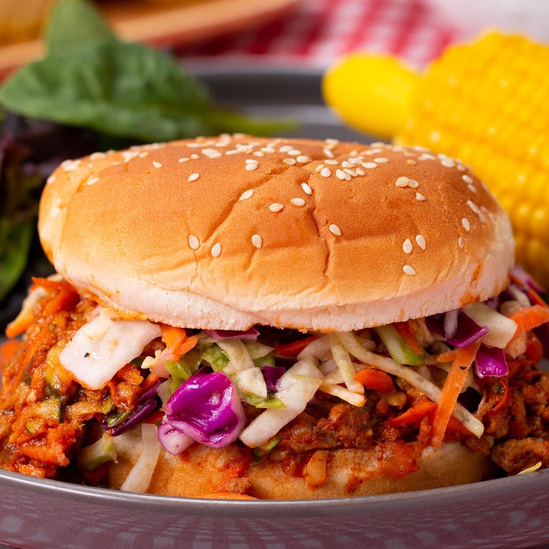 A sloppy joe sandwich topped with coleslaw on a sesame bun, served with a side of corn on the cob