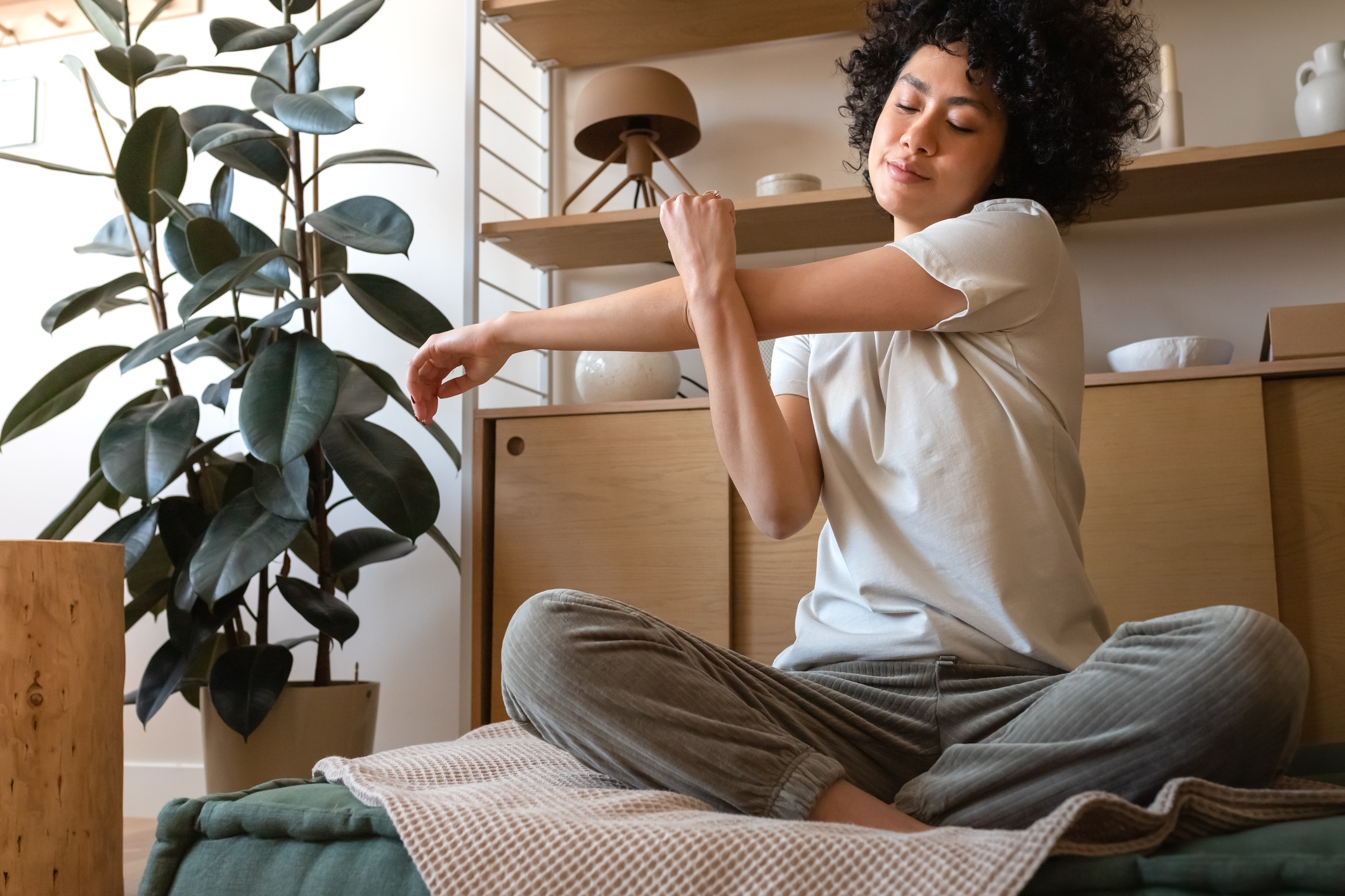Personen som gjør en sittende armstrekning i et koselig, plantefylt rom. Uformell loungewear forbedrer den avslappede atmosfæren