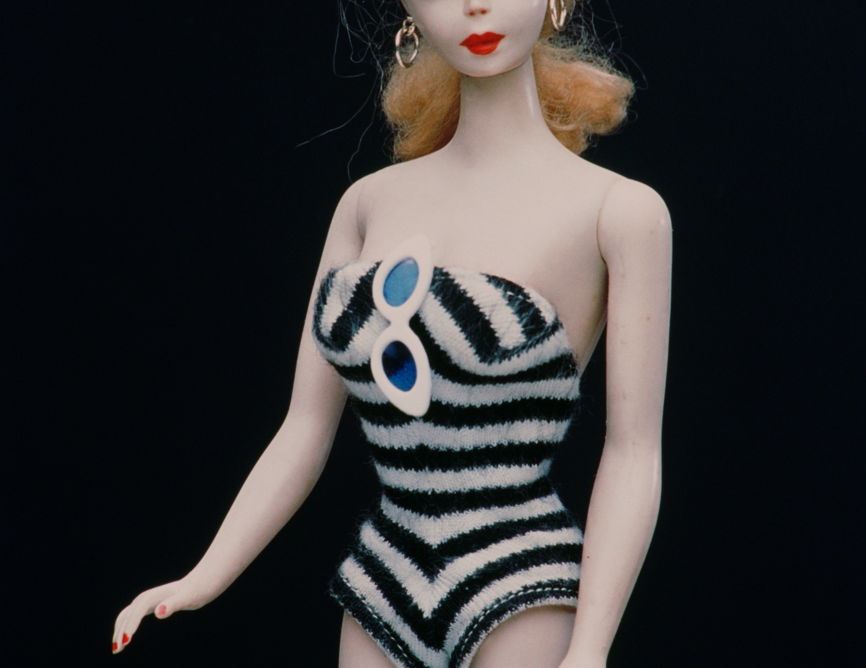 Vintage Barbie doll wearing a striped swimsuit with hoop earrings, showcasing a classic fashion design